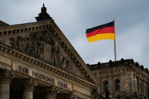 Das Bild zeigt die Fassade des Reichstagsgebäudes in Berlin mit der Inschrift „DEM DEUTSCHEN VOLKE“ und einer wehenden deutschen Flagge im Hintergrund. Diese Szene symbolisiert die politische Stabilität und wirtschaftliche Verantwortung Deutschlands – ein zentraler Aufgabenbereich der Bundesbank als Teil des wirtschaftlichen Fundaments des Landes.