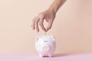Hand, die eine Münze in ein Sparschwein steckt – symbolisches Bild für Sparkonto-Optionen und Möglichkeiten, Geld zu sparen.