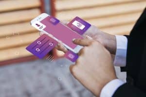 Eine Person in Businesskleidung bedient ein Smartphone mit holografisch projizierten App-Symbolen in Lila- und Rosatönen, die Funktionen wie Benutzerprofil, Einstellungen, Analyse-Diagramme und Steuerregler darstellen. Die Darstellung vermittelt ein modernes, digitales Benutzererlebnis im Finanzbereich. Diese innovative Darstellung steht sinnbildlich für die nahtlose Integration und Personalisierung von Finanzdienstleistungen im Rahmen von Open Banking.