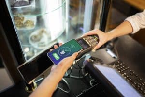 Eine Person bezahlt kontaktlos mit dem Smartphone an einem Kartenlesegerät in einer Bäckerei – eine typische Anwendung Virtuelle Karten für sicheres und bequemes Einkaufen.