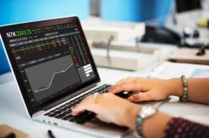 Person analysiert Finanzdaten auf einem Laptop mit Kursdiagrammen und Marktübersichten – symbolische Darstellung des Online-Handels mit ETFs und anderen Anlageformen.