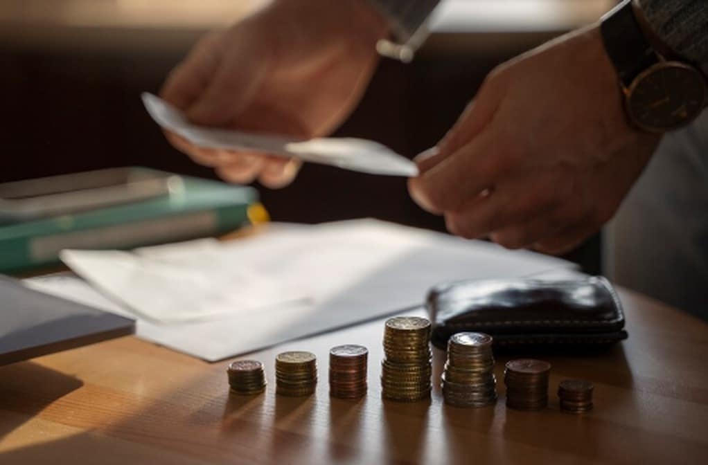 Gestapelte Münzen, eine Geldbörse und ein Dokument auf einem Tisch, während eine Person Papiere sortiert – symbolische Darstellung von persönlicher Finanzplanung und Investitionen im Rahmen des German Direct Treasury.