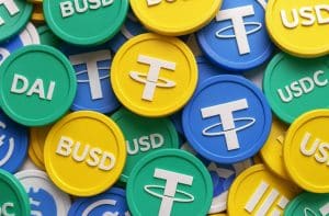 Mehrere bunte Token mit den Symbolen bekannter Stablecoins wie USDT, BUSD, DAI und USDC sind aufeinander gestapelt. Diese digitale Darstellung symbolisiert die Vielfalt stabiler Kryptoaktiva auf dem Markt. Die Szene steht stellvertretend für den zunehmenden Einsatz von Stablecoins als Kryptoaktiv im globalen Finanzsystem.