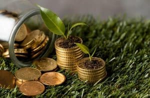 Aufeinander gestapelte Goldmünzen mit kleinen grünen Pflänzchen, die aus der Erde auf den Münzen wachsen, symbolisieren nachhaltige Investitionen und Green Bonds.