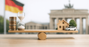 Investitionen in Deutschland dargestellt durch Waage mit Münzstapeln, Sanduhr, Haus und Auto vor dem Brandenburger Tor und deutscher Flagge.